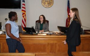 Two Mediation Clinic students are standing in front of Judge Kelly V. Wegel's desk. Judge Wegel is sitting down between the students and listening to them.